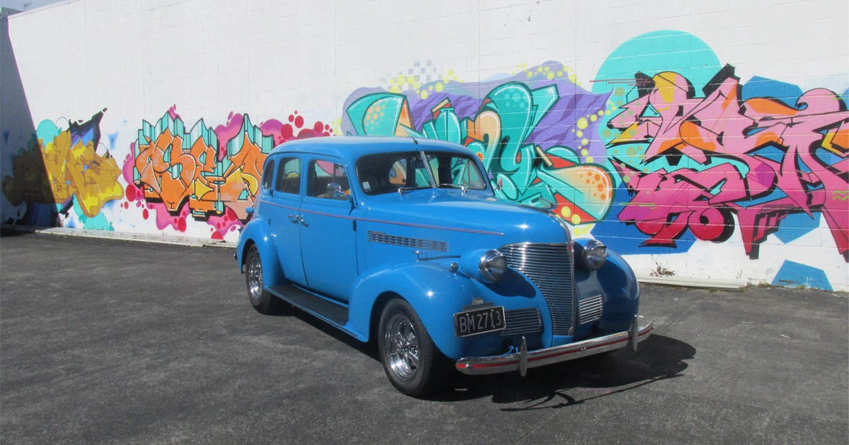a blue car parked in front of a wall with graffiti